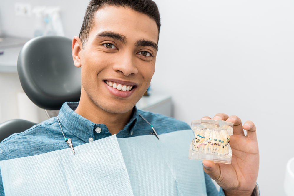 Young man smiling holding a model of teeth with braces, Longmont Braces, orthodontic diagnosis, Colorado